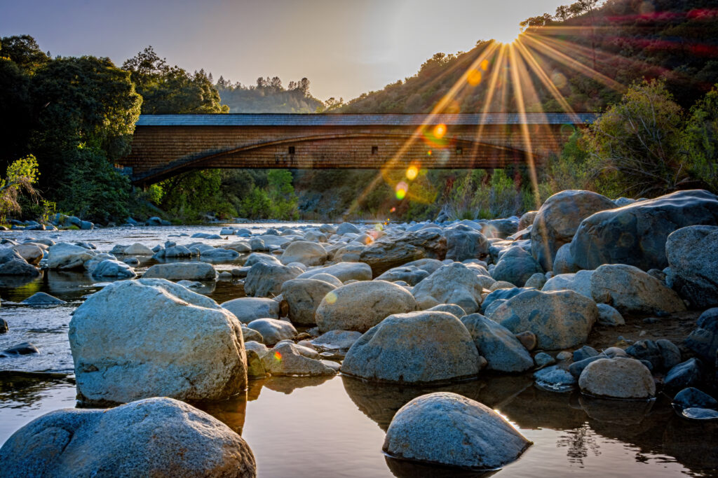 a rocky river with a view of an old brick bridge at dusk
